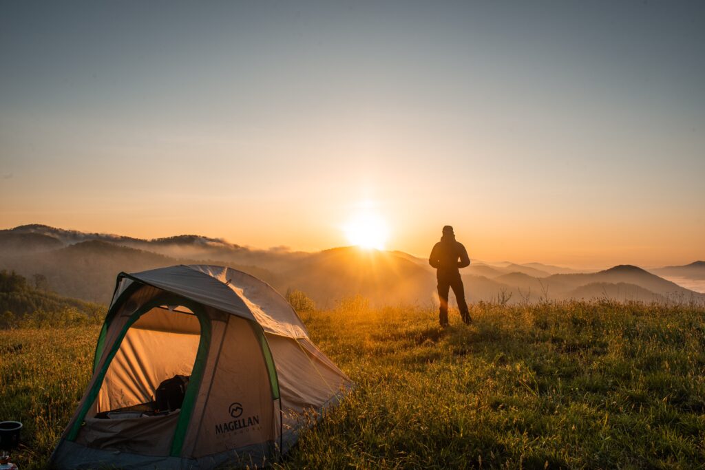 tent in mountains with woman in distance thinking about traveling to the mountains