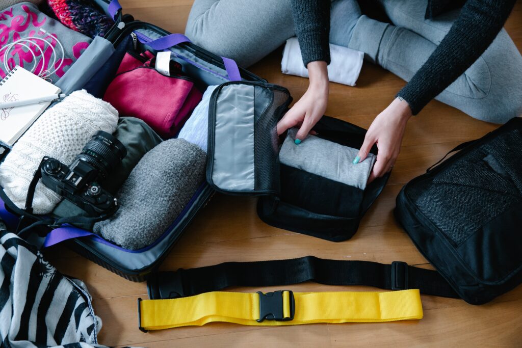 woman packing travel essentials for women into a suitcase on floor