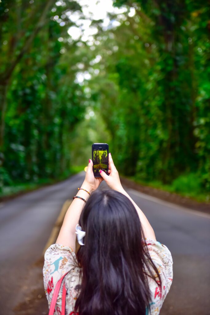 woman holds phone in wooded area and weighs pros and cons of traveling alone